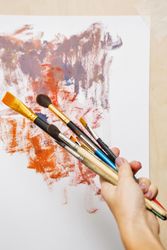 Hand holding paint brushes in front of painting