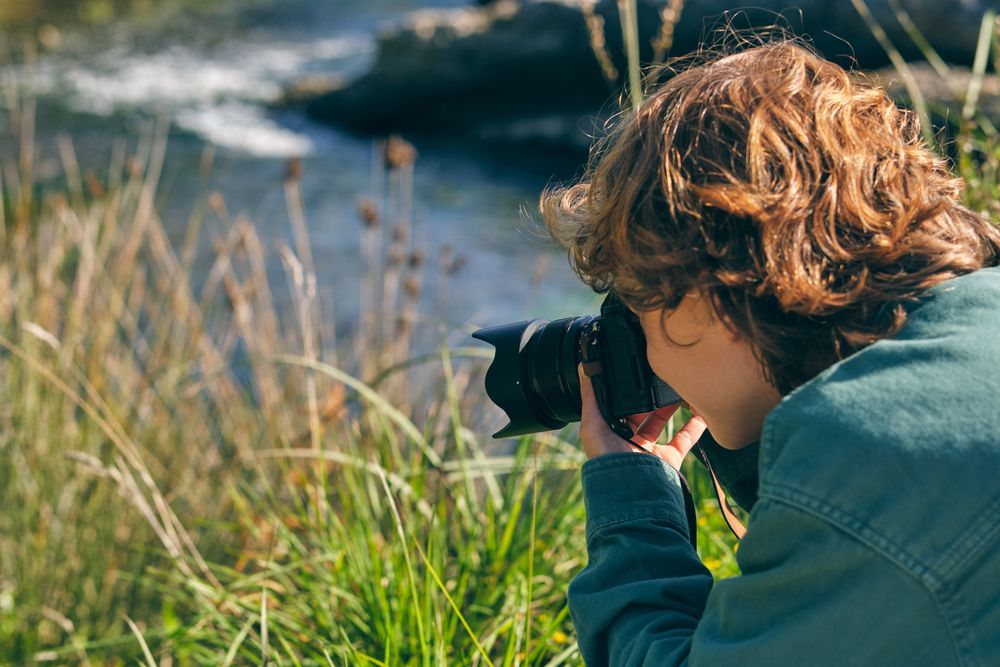 Unrecognizable boy taking photo of nature near stream of river