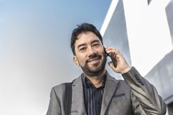 Low-angle view of an businessman talking on the cell phone while looking at camera in the street.