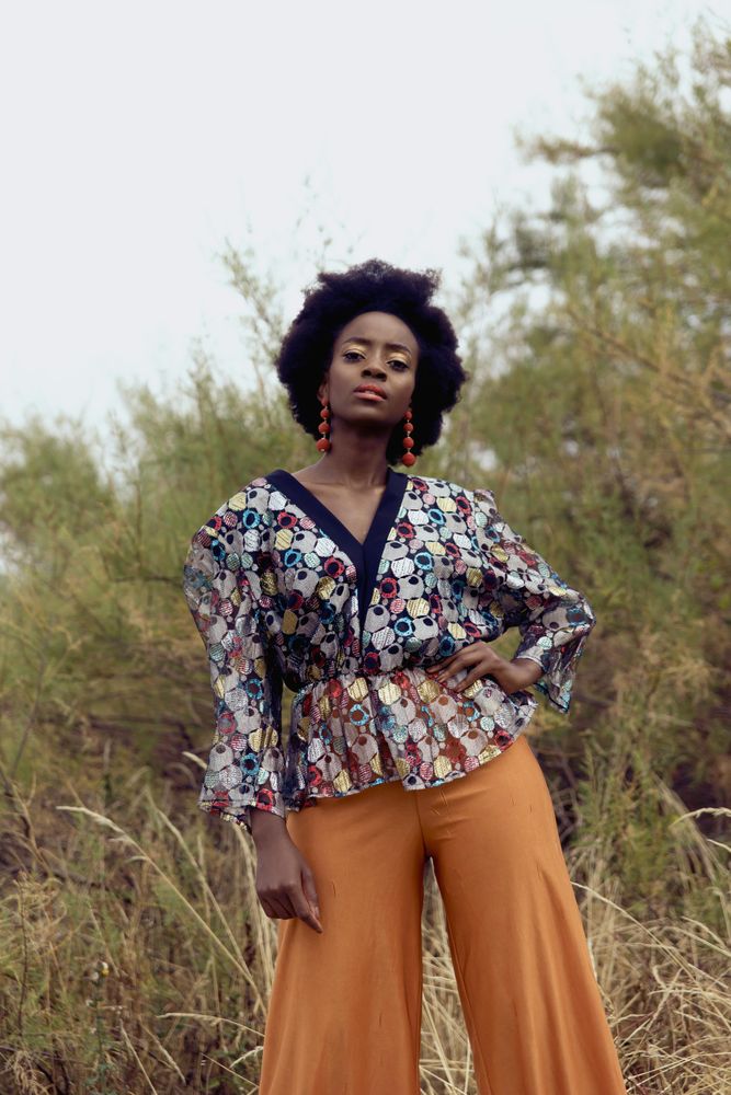 Woman in colorful patterned top and brown pants standing on green grass field