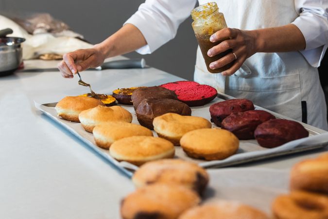 Crop cook adding jam on sponge cakes in bakehouse