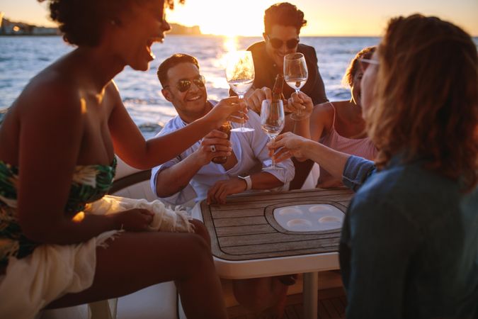 Diverse group of men and women toasting glasses while sitting at table on yacht
