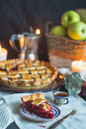 Freshly made cherry pie on table with basket of apples