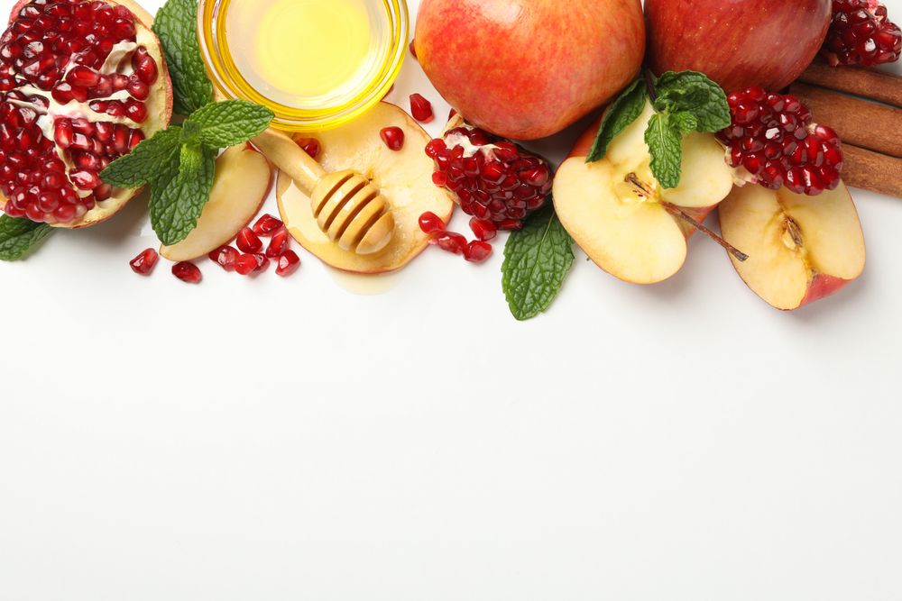 Glass honey pot with dipper, pomegranate, and an apple quarters with copy space