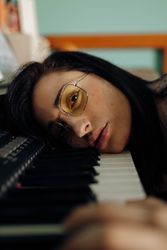 Young woman in sunglasses lying on piano
