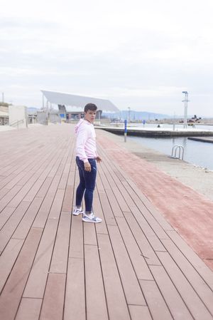 Young male teenager walking along rocky breakwater and looking back at camera