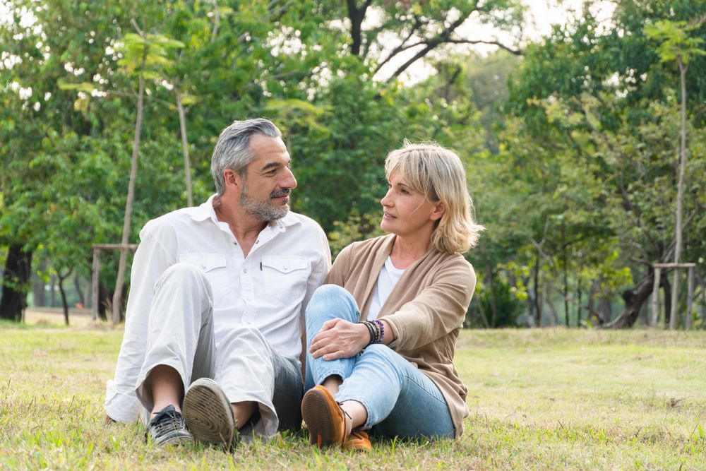 Mature male and female sitting in the grass in public park