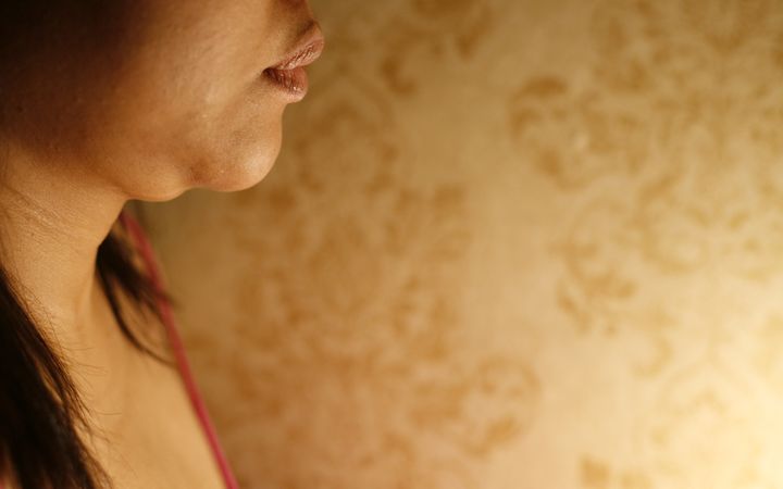 Side view of woman’s neck and  against wall paper