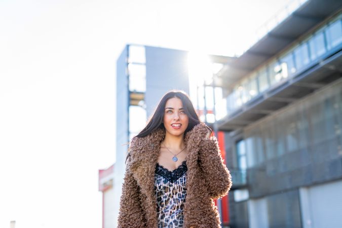 Cheerful woman wrapping in coat on street