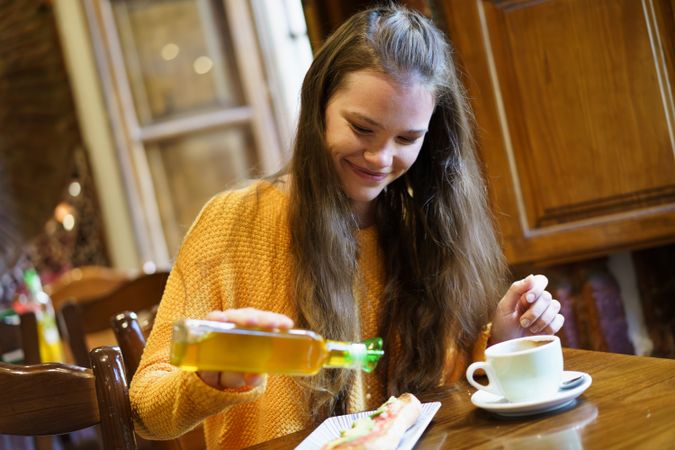 Young Woman Enjoying a Meal with Olive Oil and Coffee in a Cozy Caf