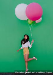 Joyful young woman jumping up holding a bunch of balloons 48a6jb