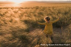 Young girl in yellow dress walking in tall grass field at sunset 4M88E5