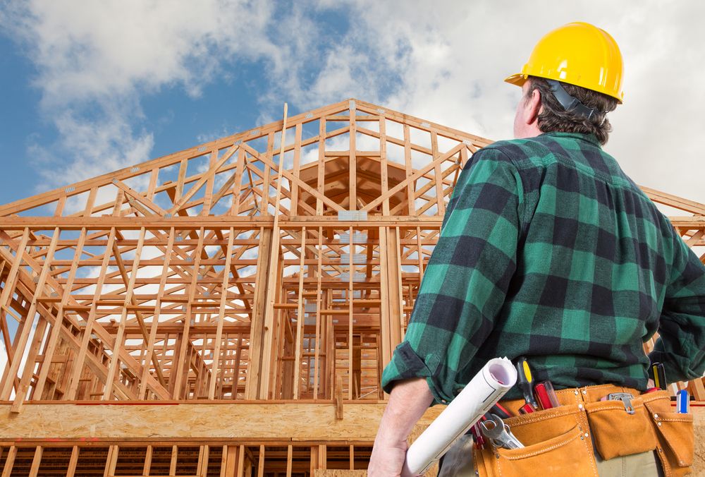 Contractor Wearing Hard Hat Standing In Front of New House Wood Framing at Construction Site.