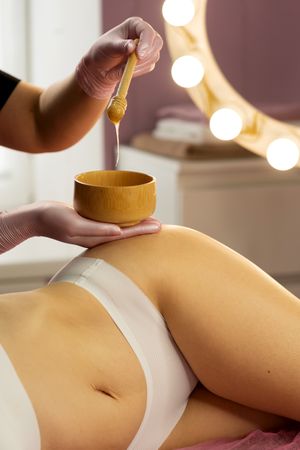 Beautician holding bowl and stick with honey during treatment.