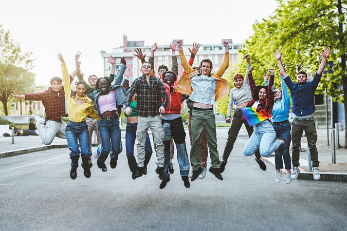 Group of happy multi-ethnic adults aged 18-20 jumping and smiling in the street with raised hands