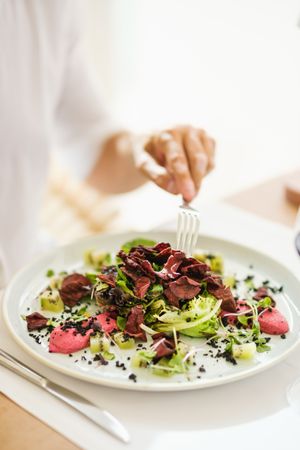 Crop person eating salad in light room