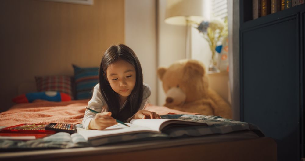 Cute South Korean Small Girl Making a Kid's Drawing of a Family Portrait with Colorful Pencils.