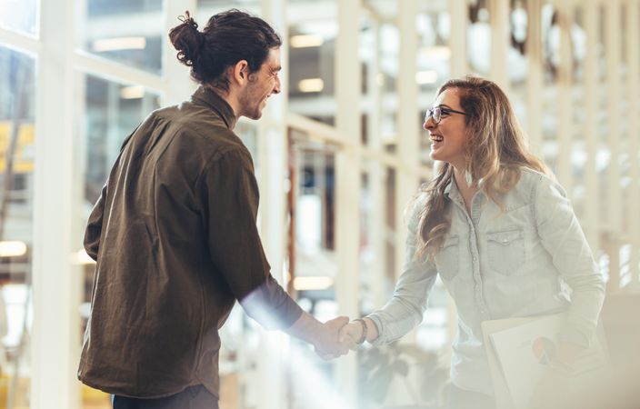Happy business colleagues greeting each other by shaking hands at workplace