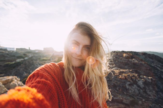 Blonde woman in red sweater taking selfie on a hill