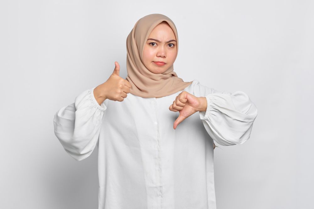 Asian female in headscarf with with hands making alternate thumb gesture