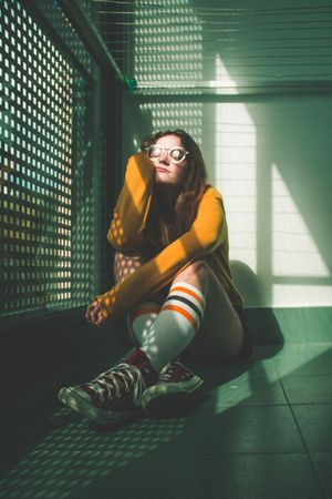 Girl wearing eyeglasses and converse sitting on floor indoor