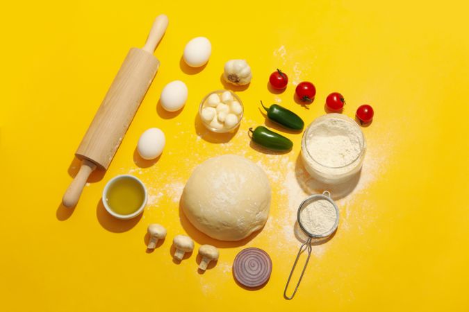 Dough and ingredients for cooking pizza on yellow background