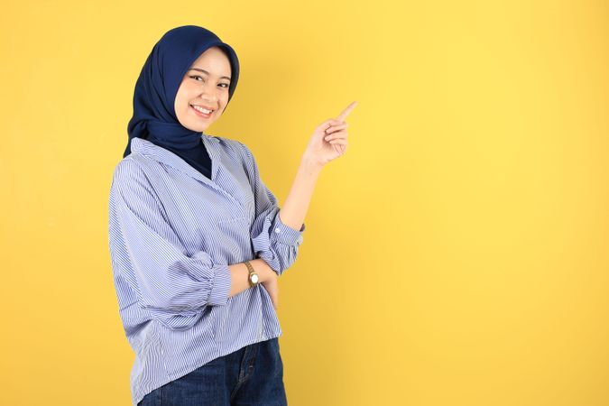 Smiling Beautiful Asian Young Woman in Blue Striped Shirt and Navy Jilbab Pointing Fingers Aside