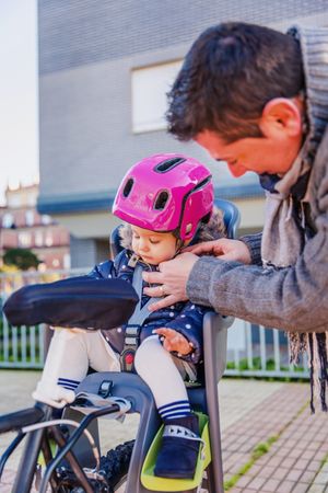 Portrait of father securing pink helmet on daughter in bike seat