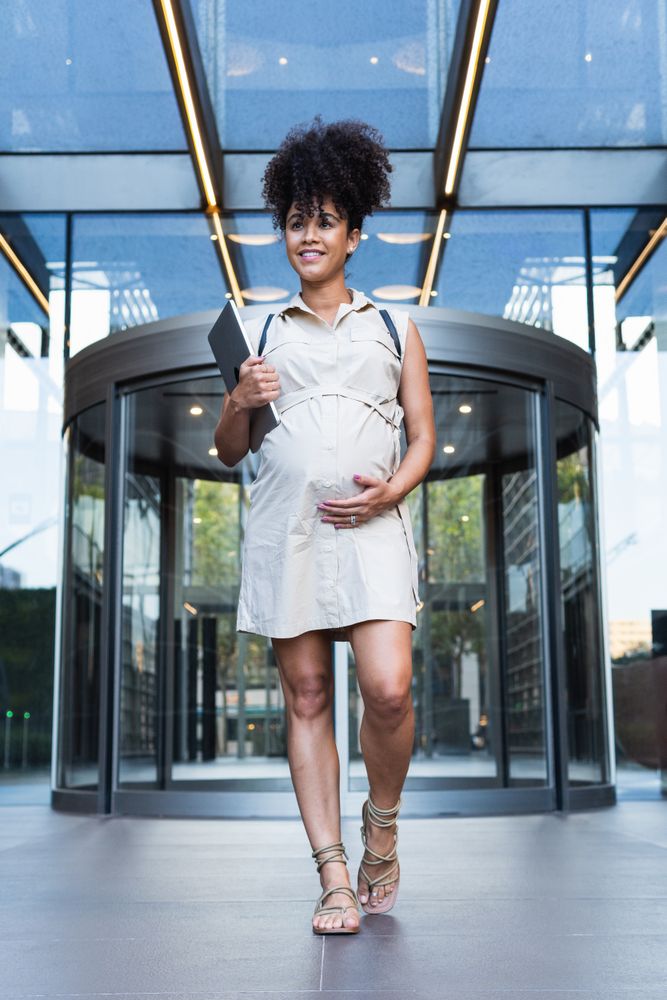 Smiling Black woman with laptop coming out of office building