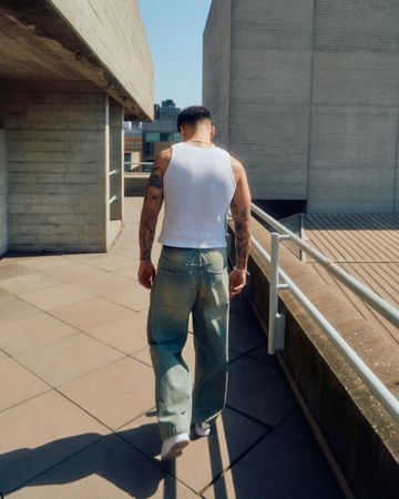 Back of man in vest and jeans walking among concrete structures