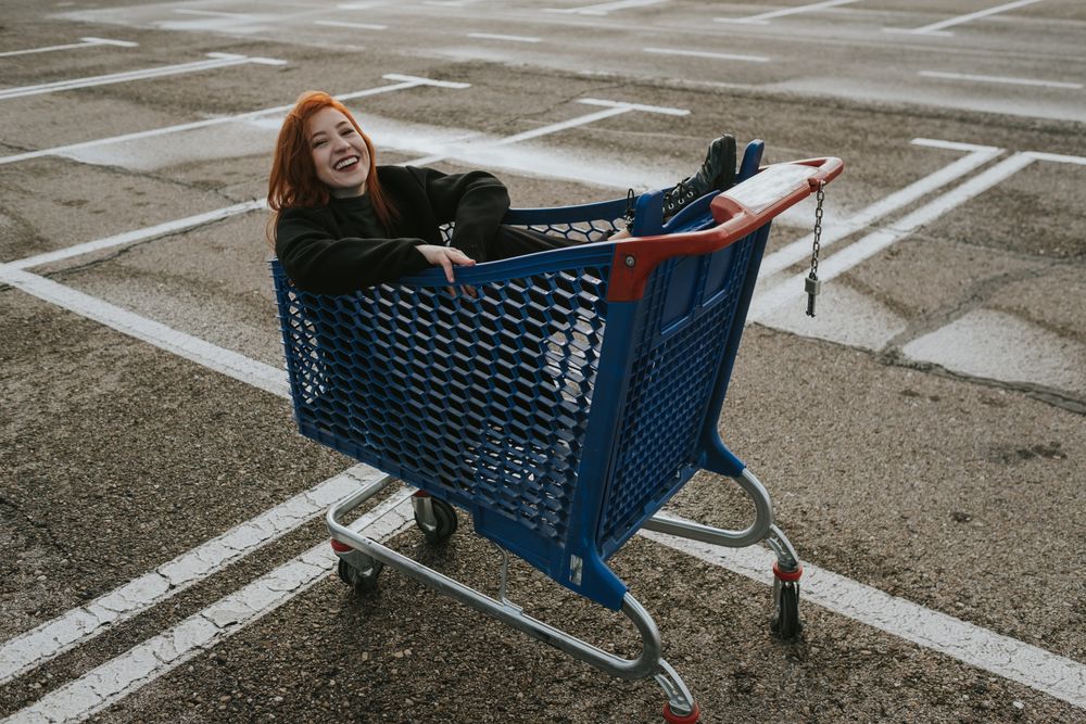 Smiling woman sitting in shopping trolley in parking lot