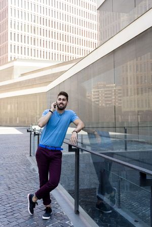 Man leaning on glass railing outside talking on mobile phone