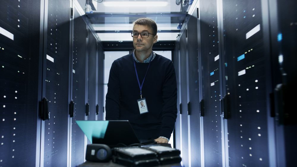 Shot of Server Engineer Pushing Crash Cart with Laptop, Hard Drives and Hardware Through Data Center.