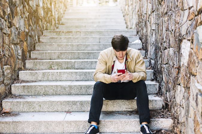 Young man using mobile phone while sitting in stairs outdoors