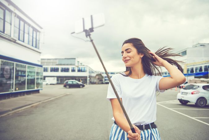 Woman with selfie stick and eyes closed outside on cloudy day