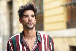 Portrait of curious dark haired man standing outside looking in the distance