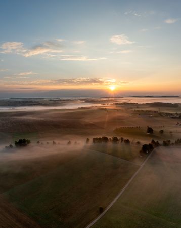 Drone aerial view with rural scenery, rolling hills covered in fog at golden hour