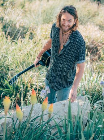 Hipster man in jungle with guitar
