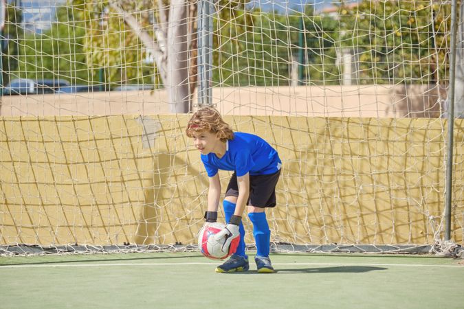 Boy standing at football goal with ball in hands
