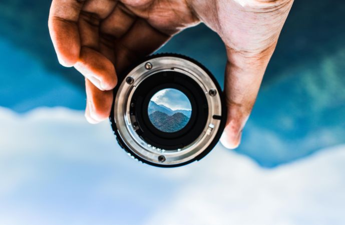 Person holding camera lens showing mountain
