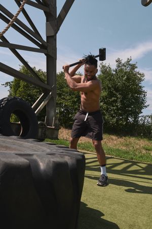 Muscular Black guy hammering tire in outdoor gym