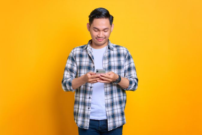 Content Asian male looking down at his phone in studio shoot