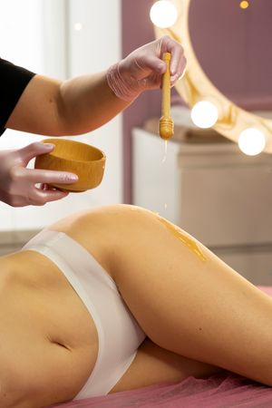 Warm honey is applied across client’s thigh during spa session.