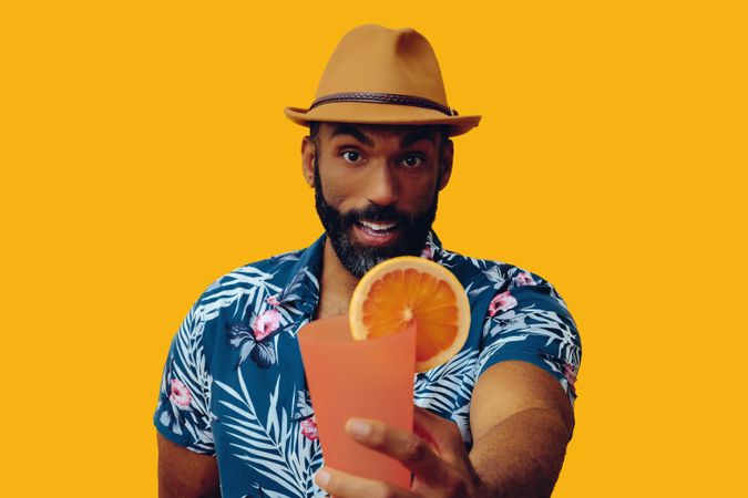 Male eagerly passing a cocktail while wearing colorful shirt with yellow background