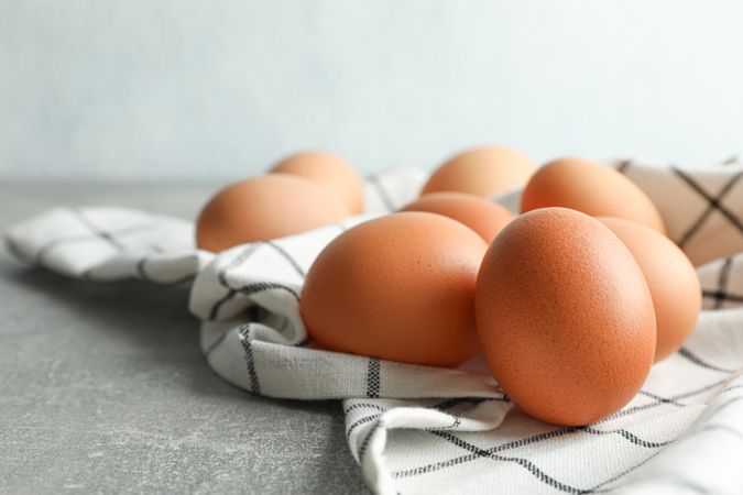 Brown chicken eggs in kitchen towel on grey table against light background, space for text and closeup