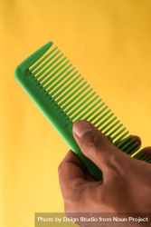 Hand holding bright green hair comb diagonally against yellow background 5qkqro