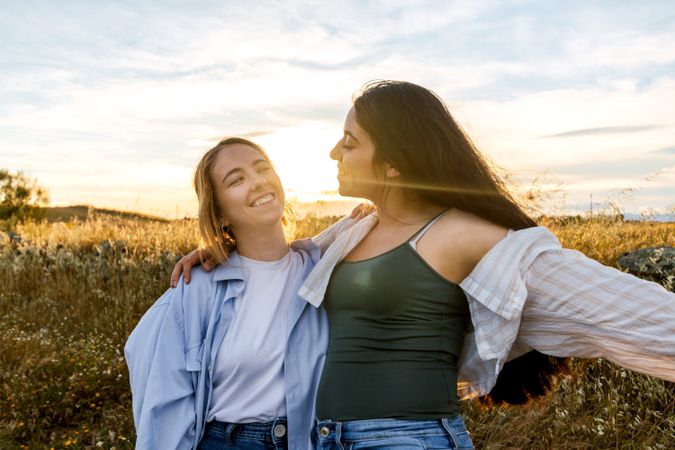 two young women looking each other on a field during sunset