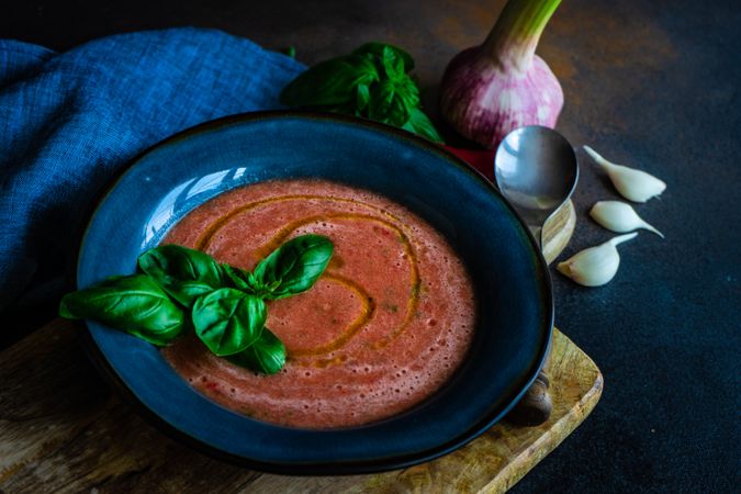 Traditional Spanish gazpacho with basil leaf and olive oil garnish in blue bowl