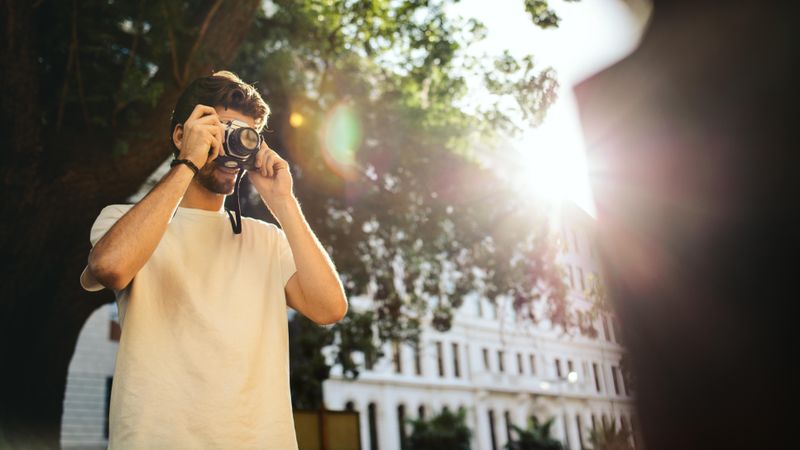 Man taking a photo with the camera close to his face and sun flare in the background