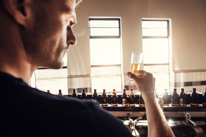 Young man examining craft beer sample glass in manufacturing factory